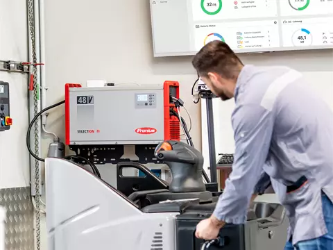 A man is connecting a forklift truck to a SelectION lithium-ion battery charger for charging.