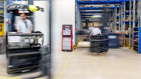 Men driving a forklift truck in front of a SelectION lithium-ion battery charger.